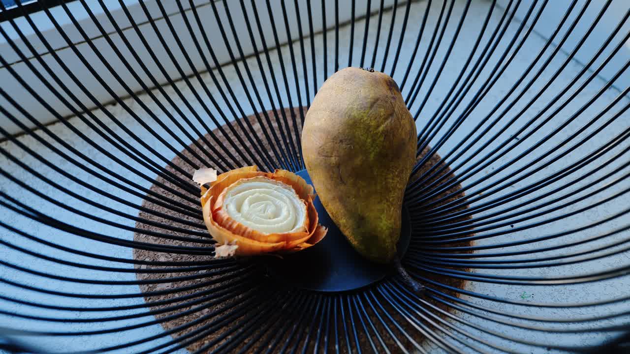 Pear and onion in wire bowl emerge through wide slow motion retreat