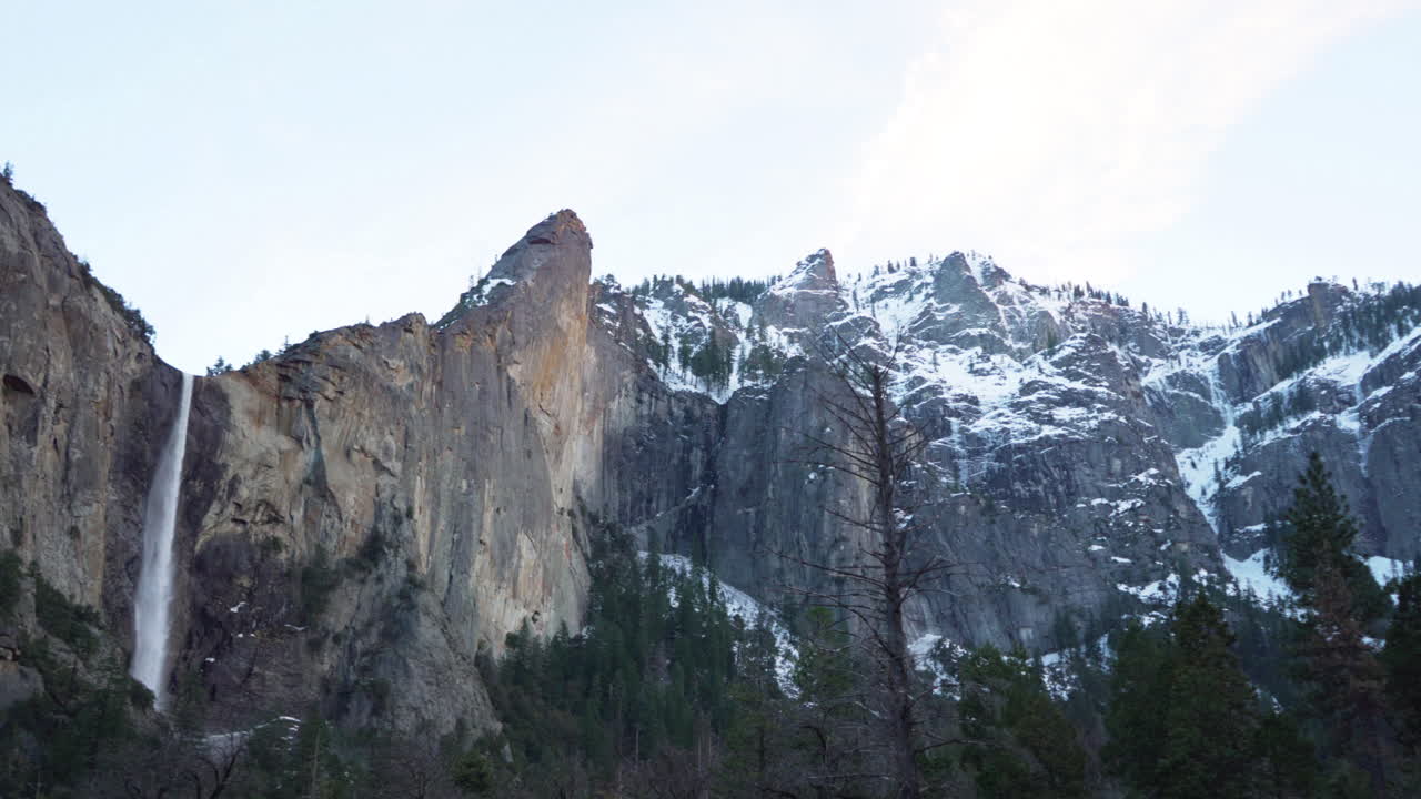 toma panorámica de picos cubiertos de nieve en el parque nacional de yosemite que revela las cataratas bridalveil después del atardecer
