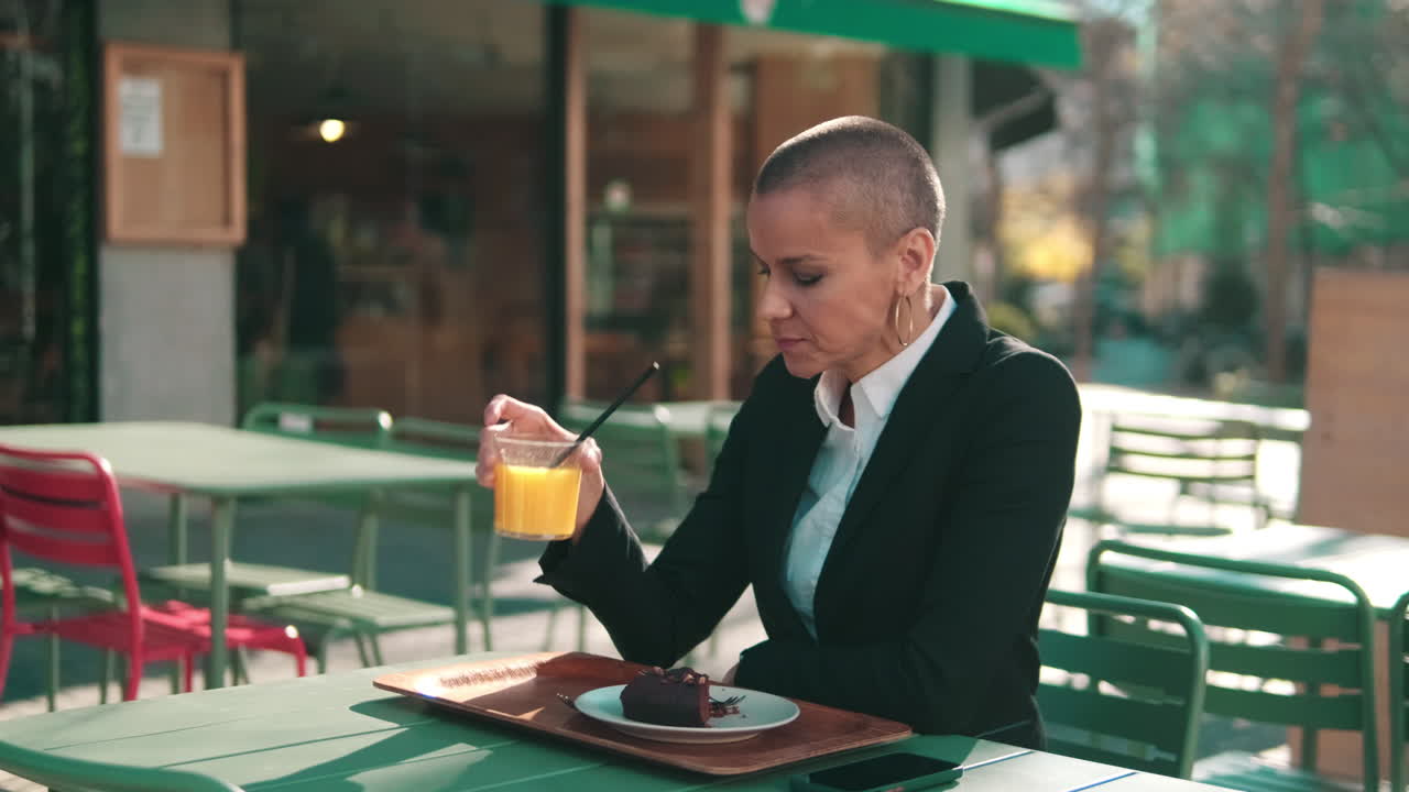 屋外カフェでオレンジジュースを飲む坊主頭の女性