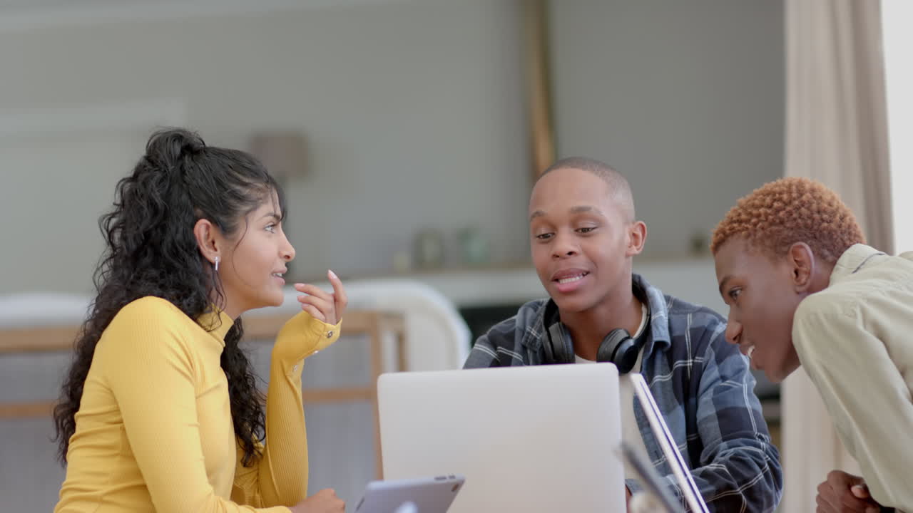 Happy diverse group of teenage friends studying at table with laptop at home, slow motion