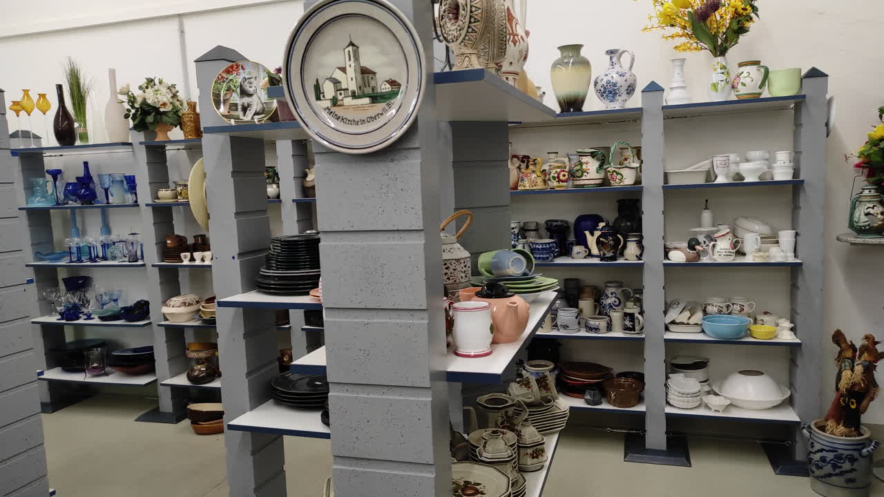Inside a thrift store in Germany. Dinner plates and other ceramics on shelves. Panning shot.
