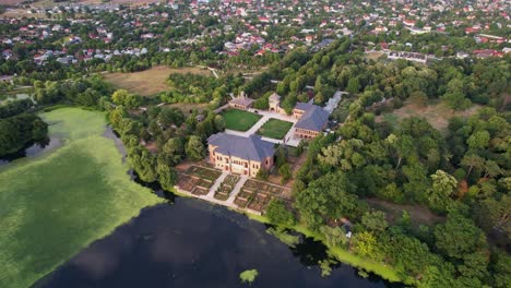 Mogoșoaia-palace-in-romania,-lush-greenery,-tranquil-lake-at-sunset,-aerial-view