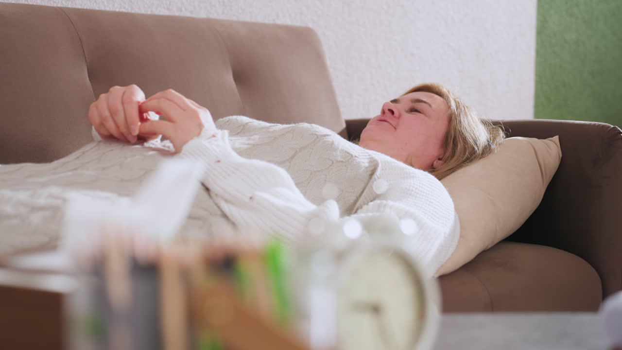 Inner explorer lying faced up on sofa with pillow support under head conversing softly in contemplative room with blurred pencils and retro clock on nearby desk creating serene therapeutic ambiance