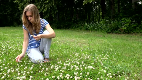 la mujer rubia se sienta en el prado teje la corona de la cabeza de las flores de la planta de trébol. 4k