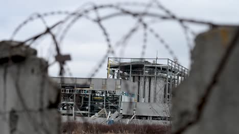 a destroyed factory on the outskirts of kramatorsk is seen through a broken fence and tangled barbed wire. a stark view of the industrial damage caused by the war in ukraine