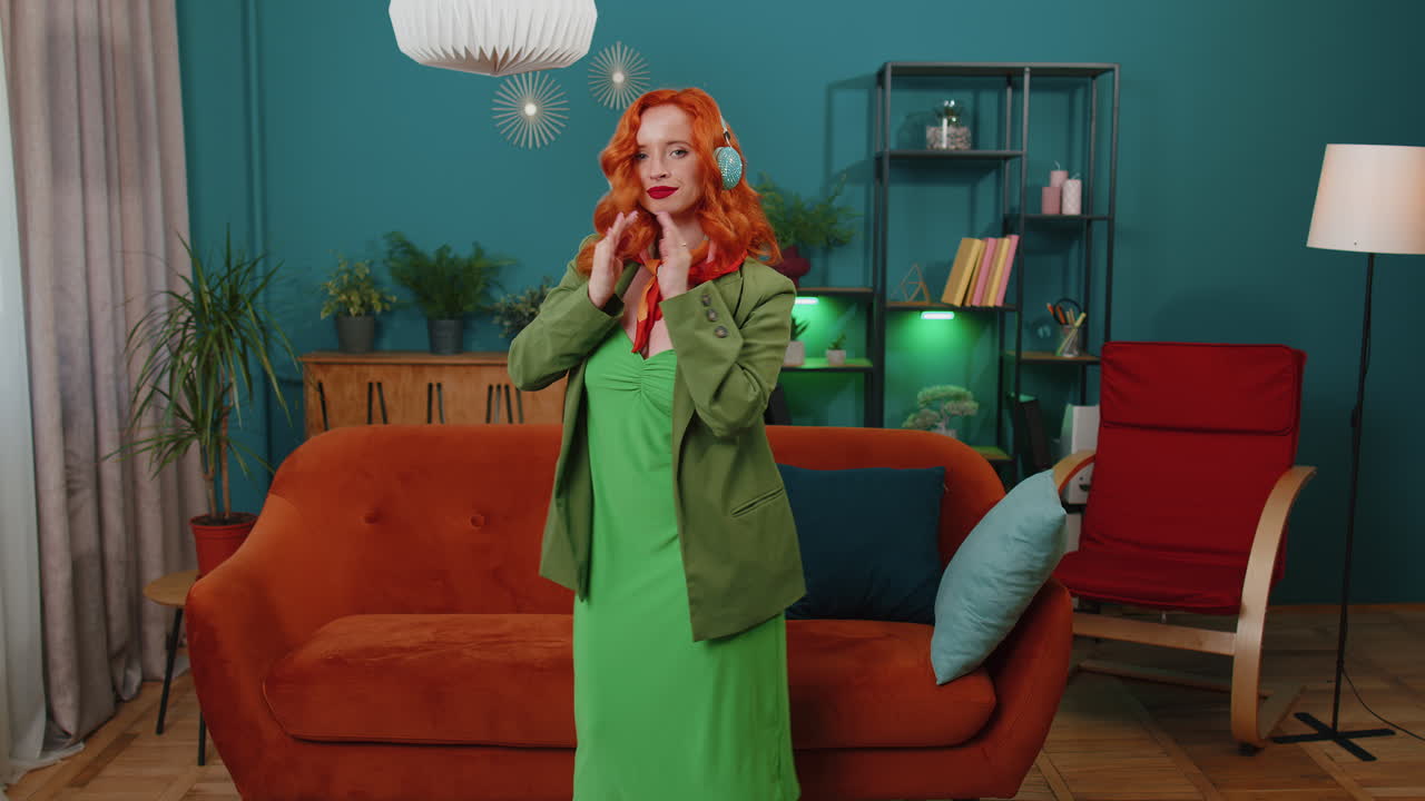 무선 헤드폰을 입은 행복하고 편안한 소녀가 춤을 추고 집 소파에서 좋아하는 록 앤 롤 음악을 듣고 있습니다.