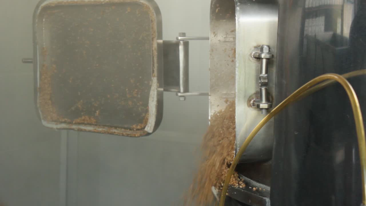 close up of a man taking out the grain husks from the kettle with a wood spoon after boiling, craft beer brewing process