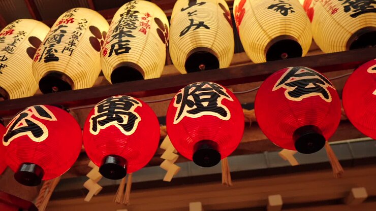 Un'inquadratura panoramica dal basso che rivela lanterne giapponesi tradizionali illuminate appese presso lo storico santuario Nishiki Tenmangu a Kyoto, Giappone. Le lanterne mostrano vari caratteri giapponesi