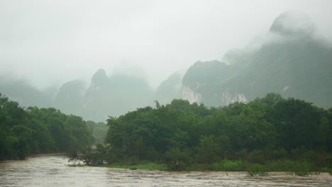 cruising on a boat along a brown river in guilin, china. watching the foggy green mountains in the background