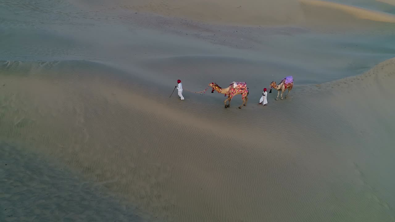 plano aéreo de dos hombres caminando con sus camellos en una duna de arena, desierto en jaisalmer, rajasthan, india