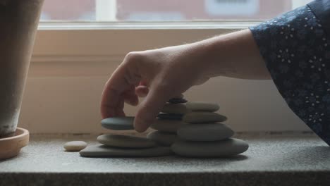 Female-hands-stacking-pebbles-on-windowsill-in-apartment,-indoors-decoration