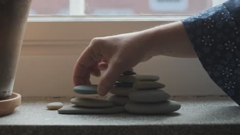 female hands stacking pebbles on windowsill in apartment, indoors decoration