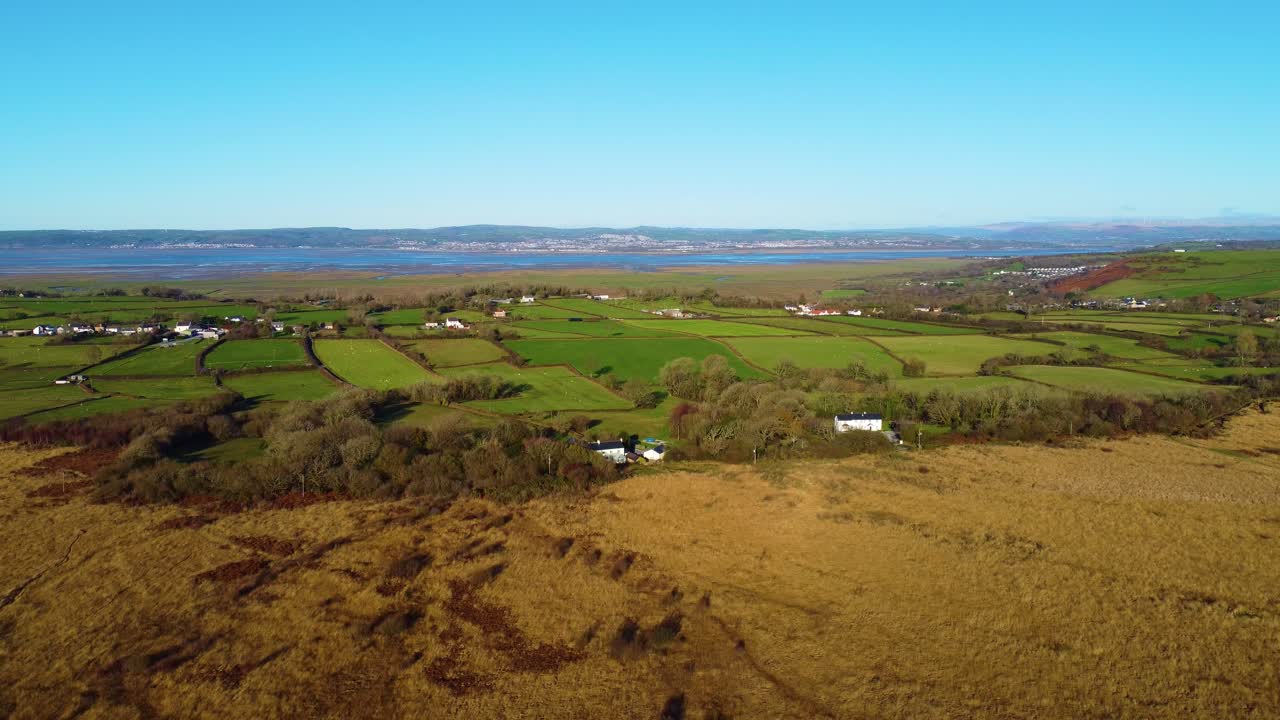 Langzaam dalende luchtopname over het platteland van Zuid-Wales met boerderijen, akkers en de Loughor-getijdenmonding op de achtergrond