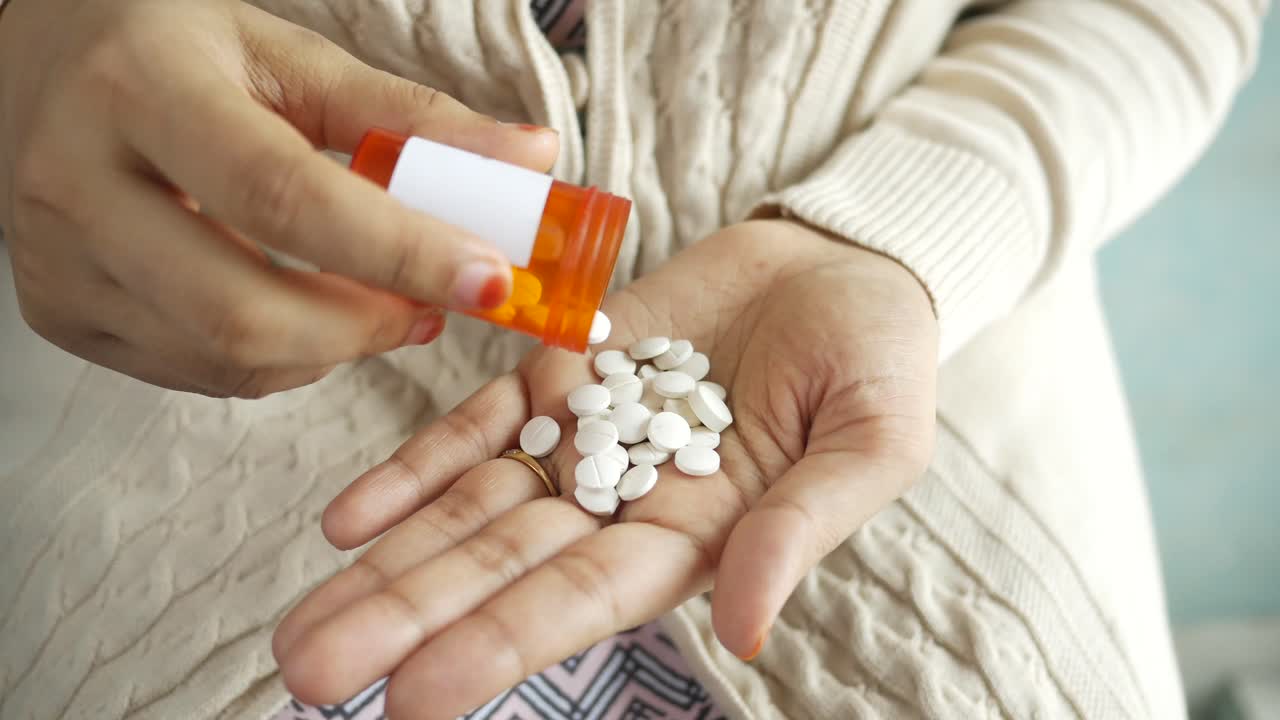 mujer vertiendo pastillas de un recipiente en su mano
