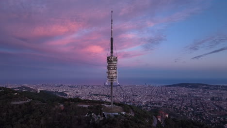 Filmische-Ansicht-Des-Collserola-Turms-Bei-Sonnenuntergang-Am-Tibidabo-Mit-Der-Stadt-Barcelona-Im-Hintergrund,-Spanien