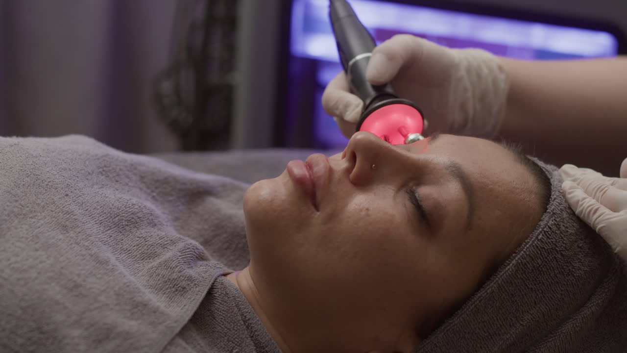 Relaxed Woman Getting Facial Massage with Red Light and Roller in Clinic