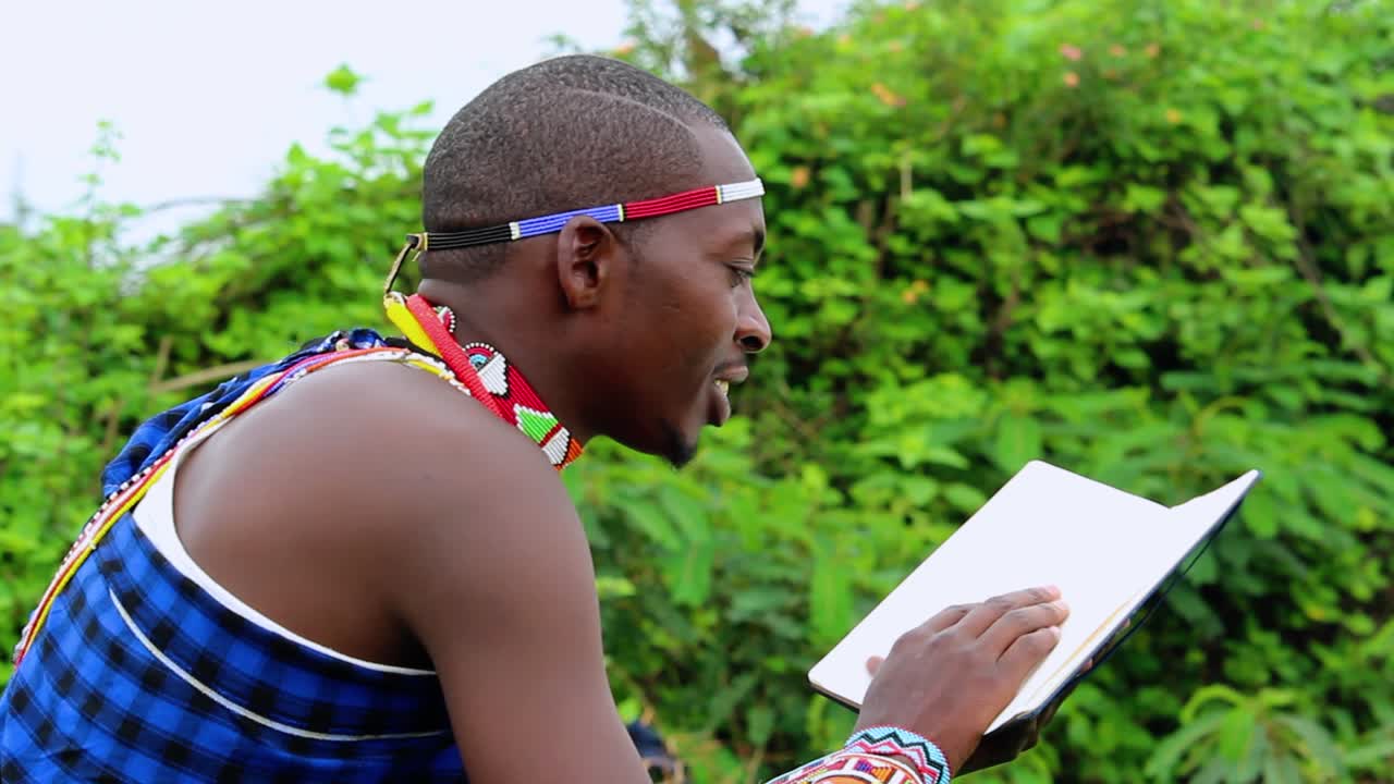 Africký muž, smějící se při čtení knihy, v džungli, v kmenovém oděvu