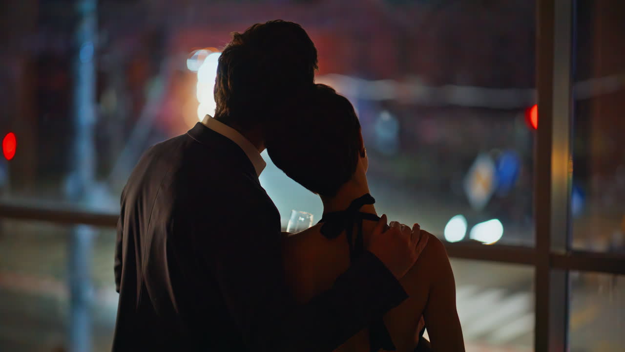 Couple embracing cityscape together with champagne panoramic window late night