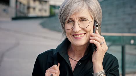 close-up portrait of happy gray-haired mature woman with smartphone. business lady is negotiating by phone