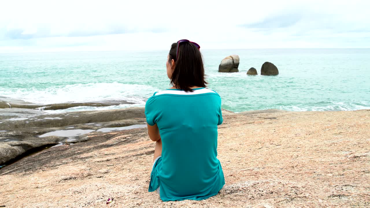 한 여인이 돌로 된 은행에 앉아 바다를 바라보고 있다.