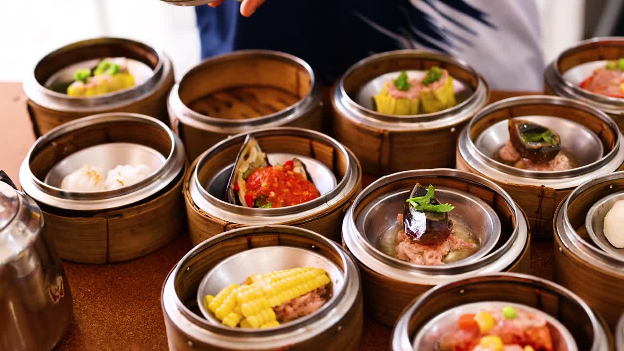 A vendor arranges colorful dim sum dishes in bamboo steamers at a bustling market in Phuket, Thailand