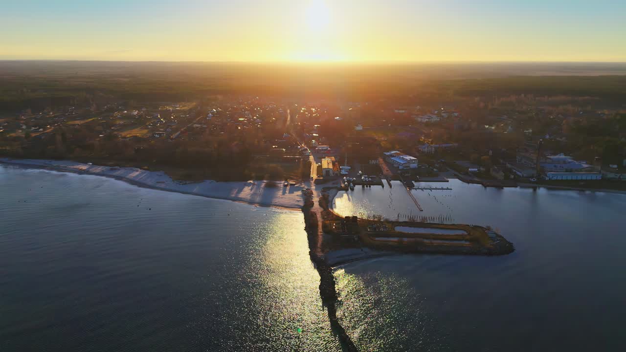 A tranquil coastal town with buildings, docks, and a harbor bathed in golden sunlight during sunrise, captured from above with soft shadows stretching inland