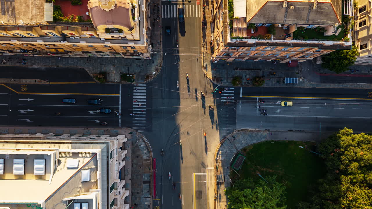 Top-down timelapse of a Genoa street at sunset, showing rooftops, cars stopping at traffic lights, moving shadows, and glowing evening light