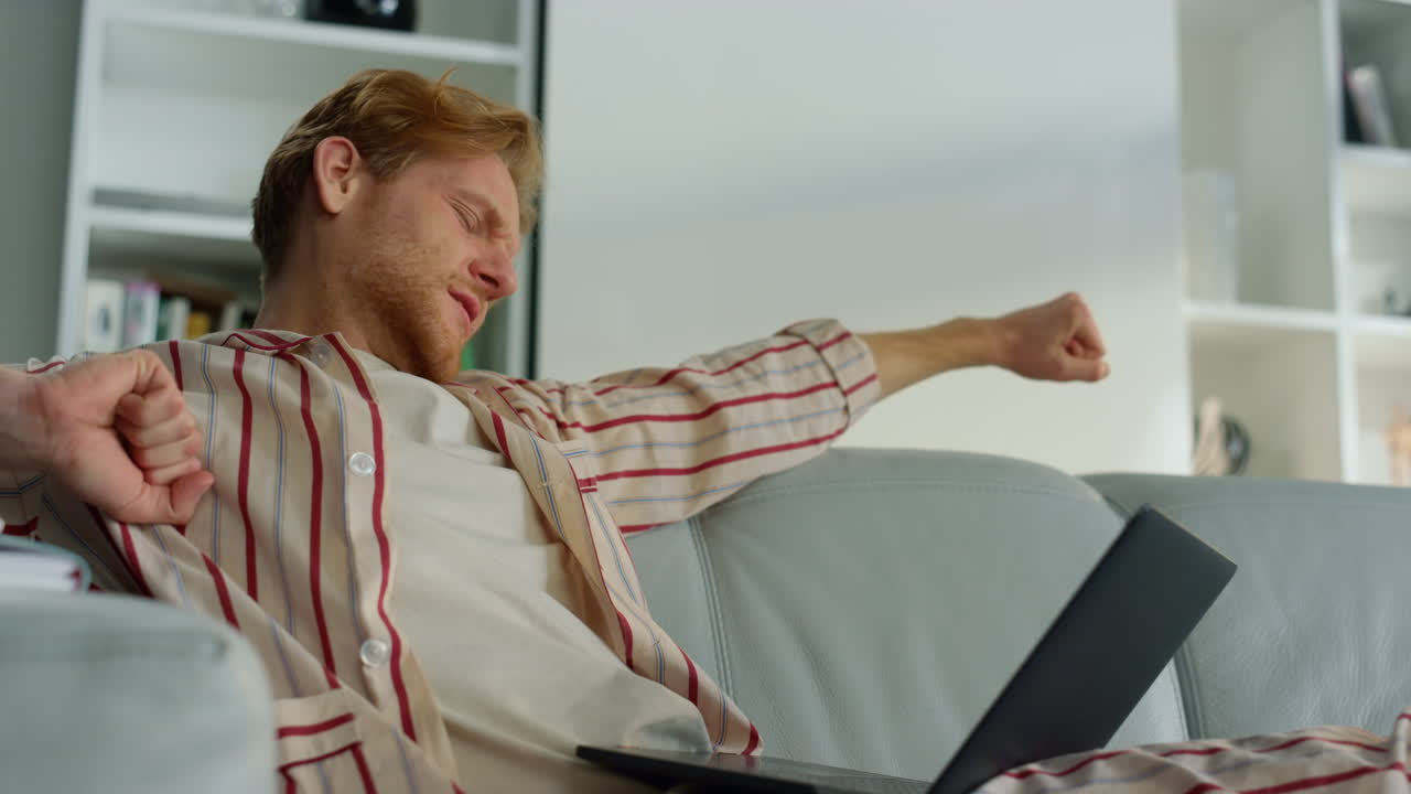 уставший парень просматривает интернет в домашнем офисе вблизи. сонный менеджер растягивает тело