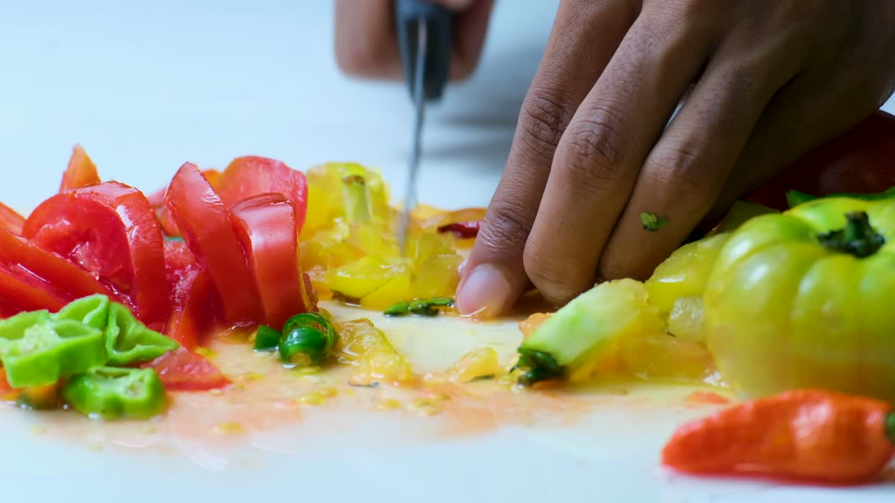 chef cortando un tomate amarillo en una superficie blanca con otros tomates picados y chiles