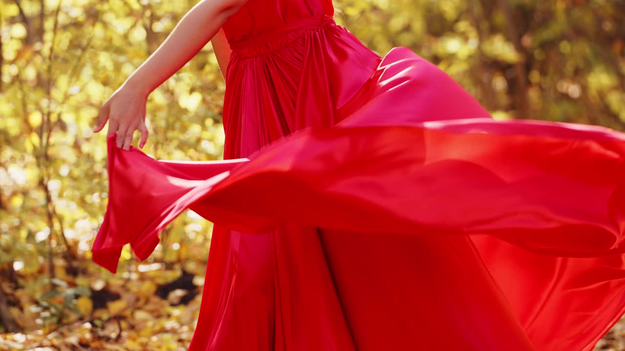 A graceful woman in a flowing red dress dances elegantly amidst a backdrop of vibrant autumn foliage, showcasing her poise and beauty in a harmonious outdoor setting