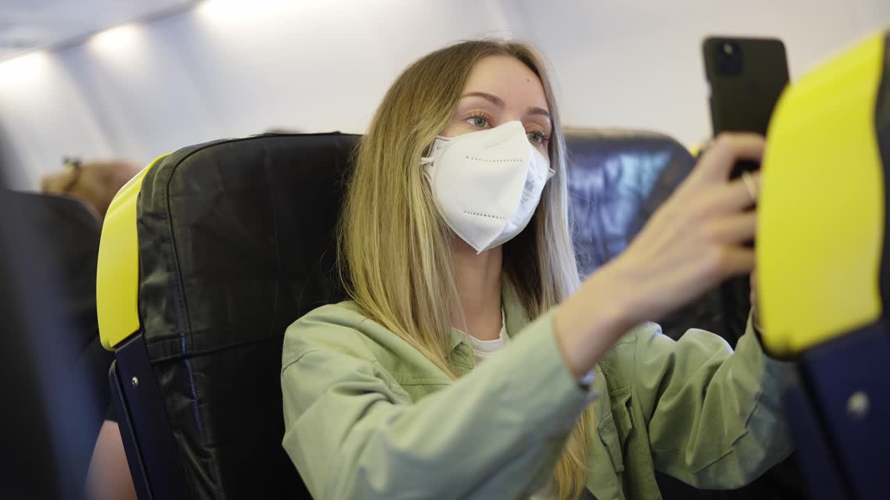 전염병 기간 동안 비행기에서 여행하는 호흡 마스크를 착용한 여성이 셀카를 찍습니다.