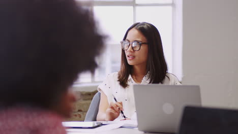 Young-Asian-female-creative-talking-with-her-colleague-in-a-meeting-room,-selective-focus