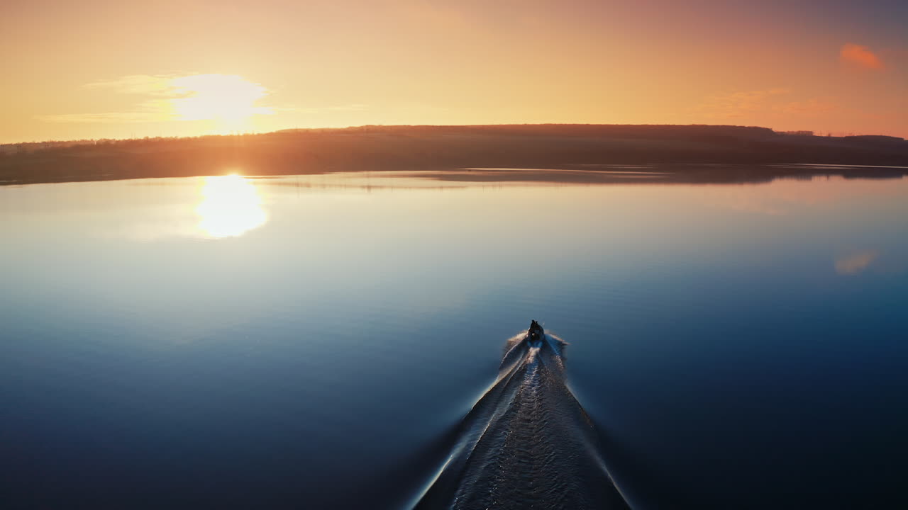 Aerial view of a motor boat at sunset. Calm water in a blue lake in the evening. People in a boat moving along the river.
