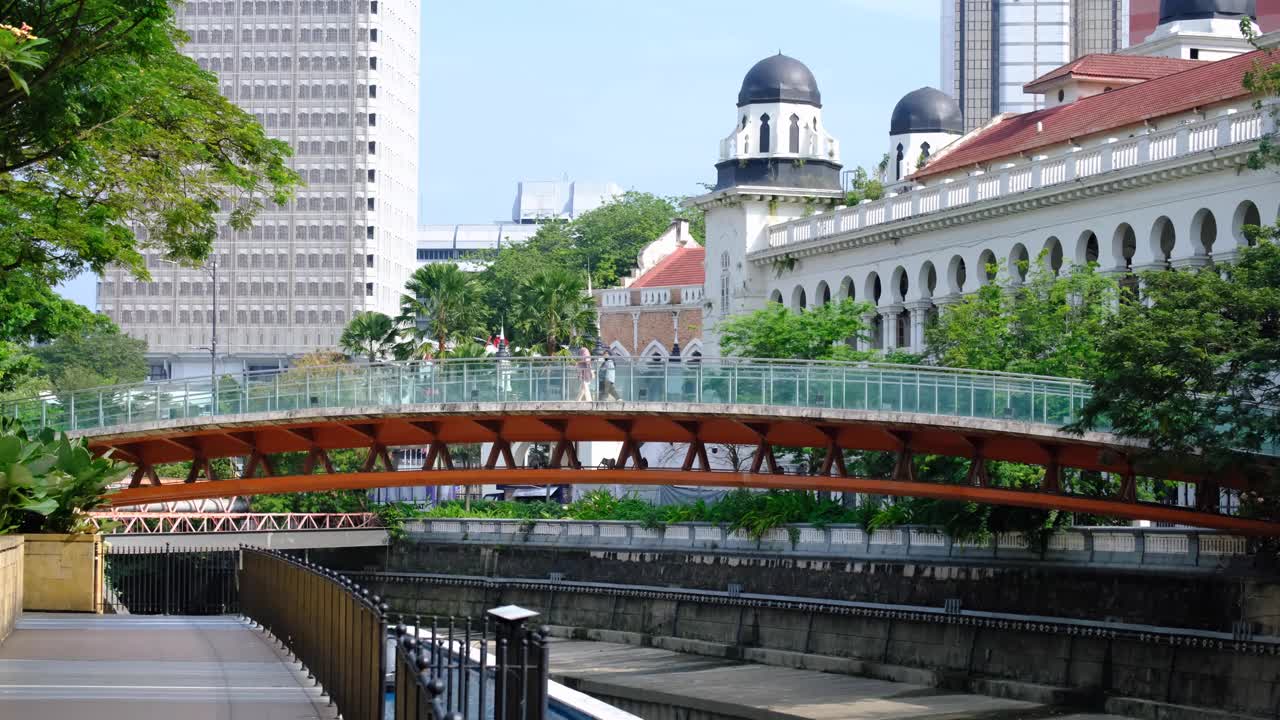 Scenic urban view of people walking on bridge over Klang River with mosque and buildings in capital city of Kuala Lumpur in Malaysia