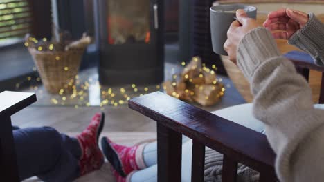 mixed race couple toasting and drinking coffee while sitting near the fireplace at vacation home