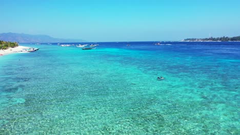 Crystal-emerald-water-of-turquoise-lagoon-where-boats-floating,-around-shore-of-tropical-island-with-exotic-beach-in-Bali