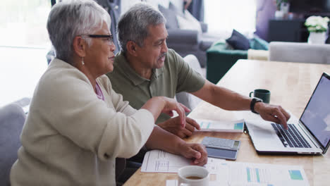 Senior-biracial-couple-talking-and-using-laptop