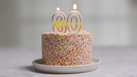 studio shot birthday cake covered with decorations and candle celebrating thirtieth birthday being blown out