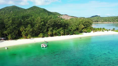 Beautiful-white-sandy-beach-under-palm-trees,-washed-by-calm-turquoise-lagoon-where-fishing-boats-floating-in-Indonesia