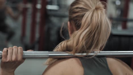 vista trasera de una mujer caucásica levantando una barra en el gimnasio.