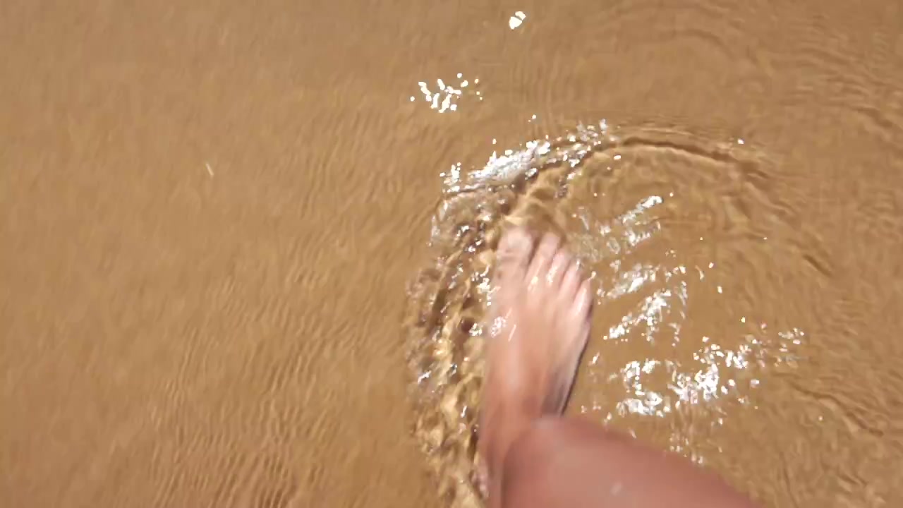 Vista in prima persona di piedi che camminano nell'acqua bassa della spiaggia