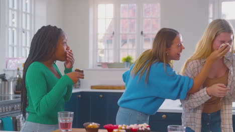 group of teenage girls eating and having fun playing with cupcakes in kitchen at home