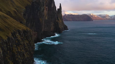 Aerial-view-following-the-steep-coast-of-Traelanípan,-the-Slave-Mountain,-sunset-in-Faroe-islands