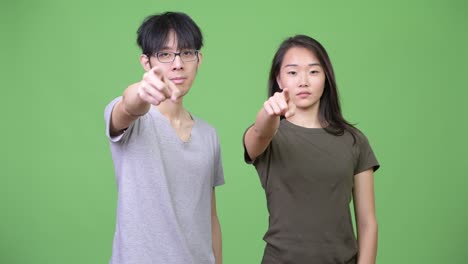 young asian couple pointing at camera