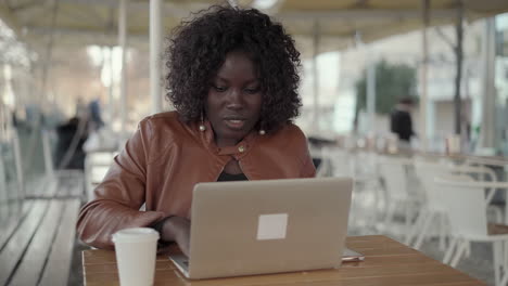 Young-female-freelancer-using-laptop-and-smartphone-in-cafe