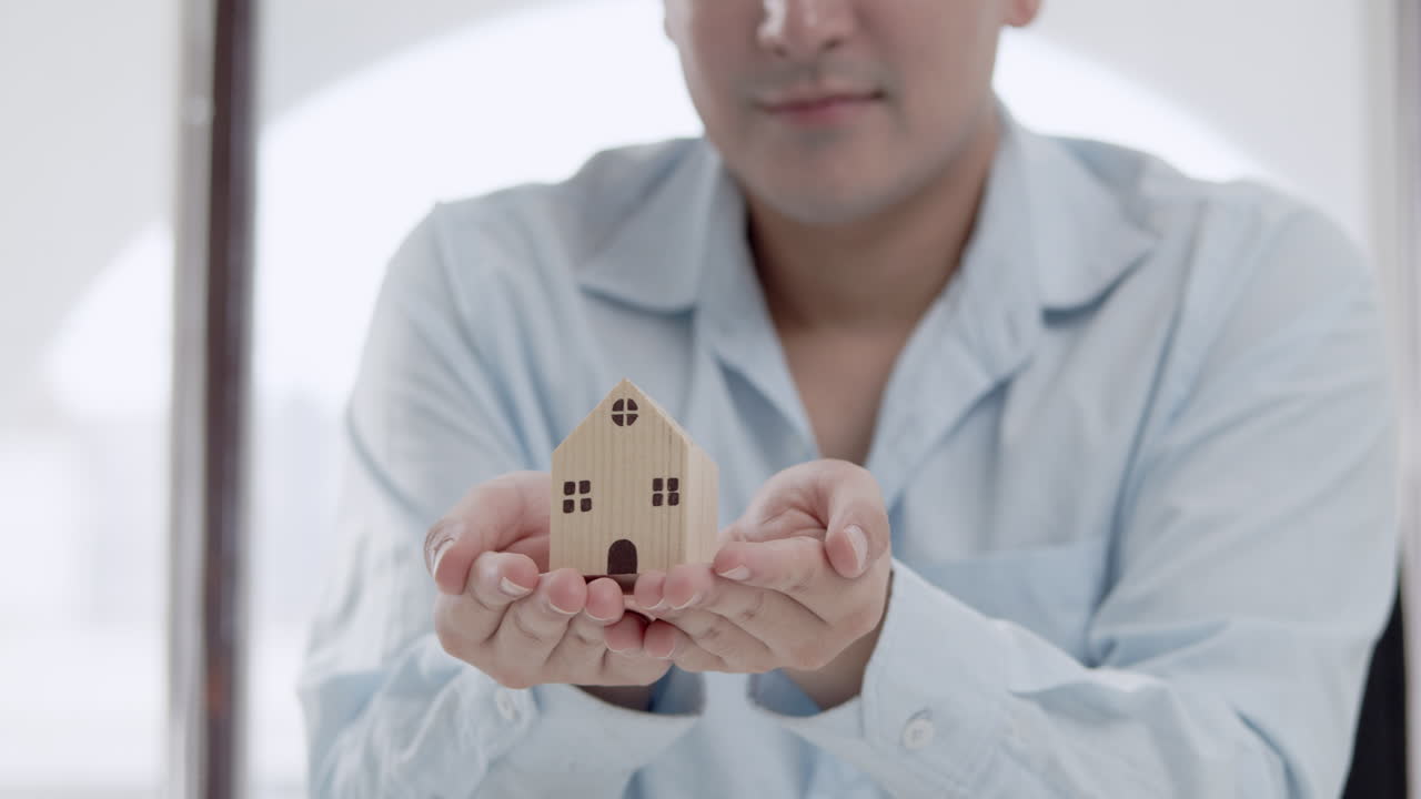 un hombre asiático mostrando una casa en miniatura para un concepto de promoción de bienes raíces y desarrolladores inmobiliarios.