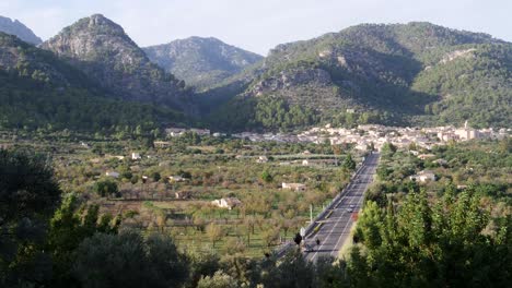 traveling cars on a serene straight road to picturesque caimari village, embraced by lush greenery and rolling hills on a beautiful autumn evening in mallorca