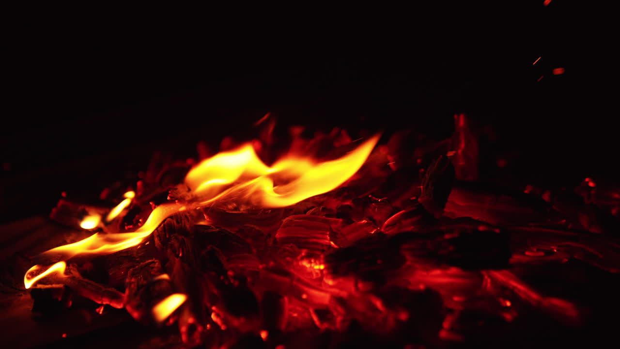 Moving the smoldering embers of burning out campfire with a stick. Beautiful sparks rise into the darkness. Close up.