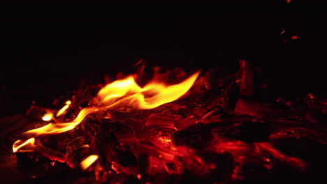 moving the smoldering embers of burning out campfire with a stick. beautiful sparks rise into the darkness. close up.