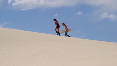 Couple-with-sand-boards-walking-on-the-sand-dune-4k